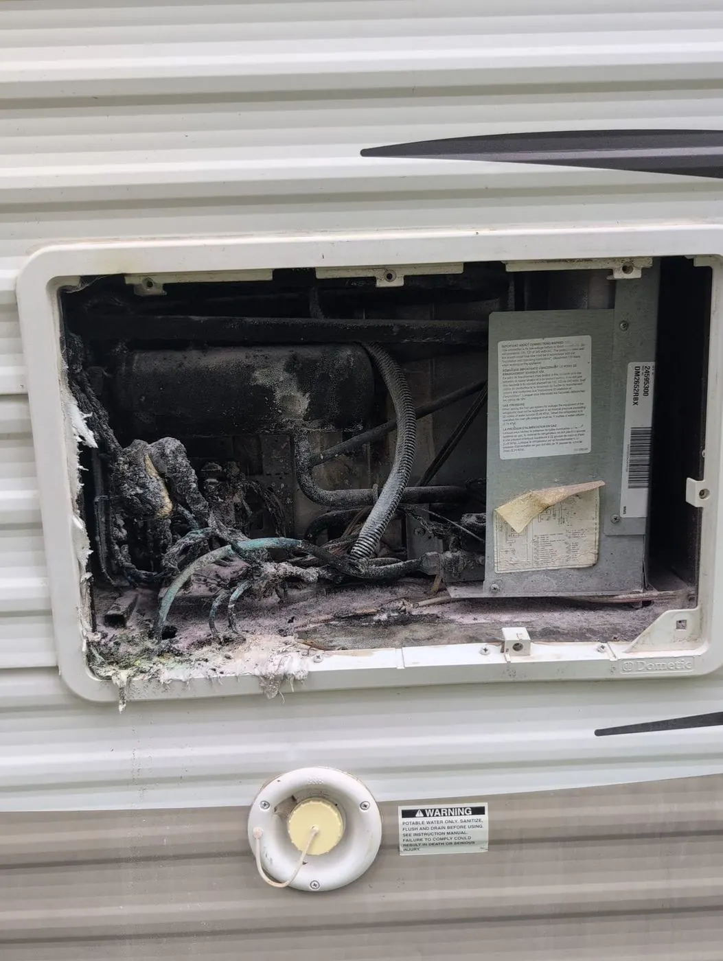RV refrigerator compartment with heavily charred and melted wiring after a fire