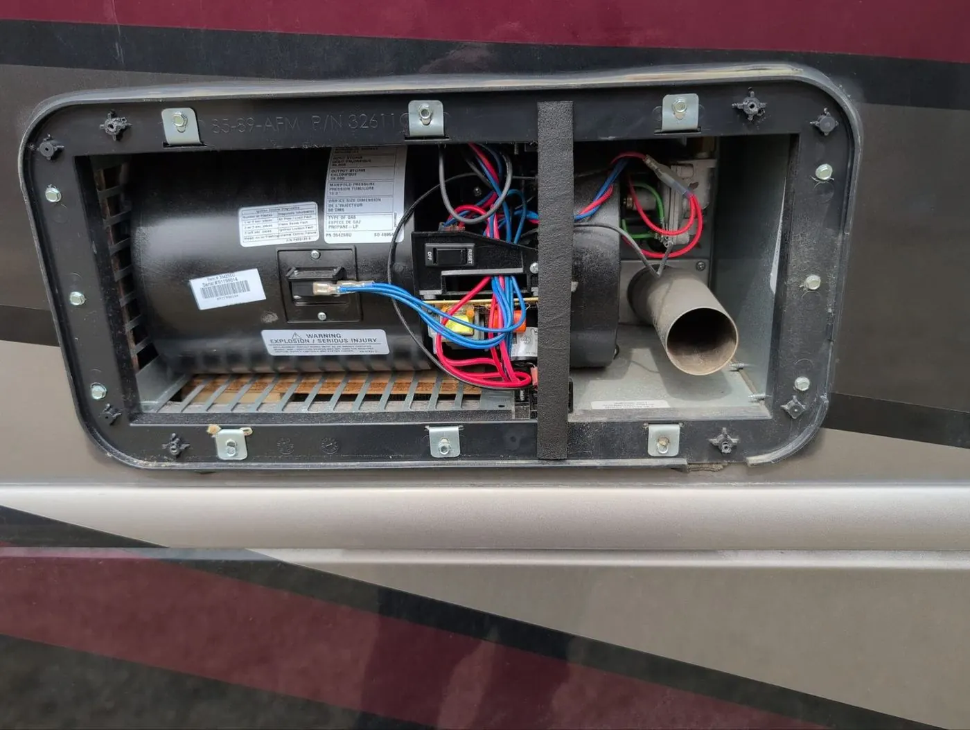 RV furnace access panel open showing the blower motor, burner, and exhaust flue