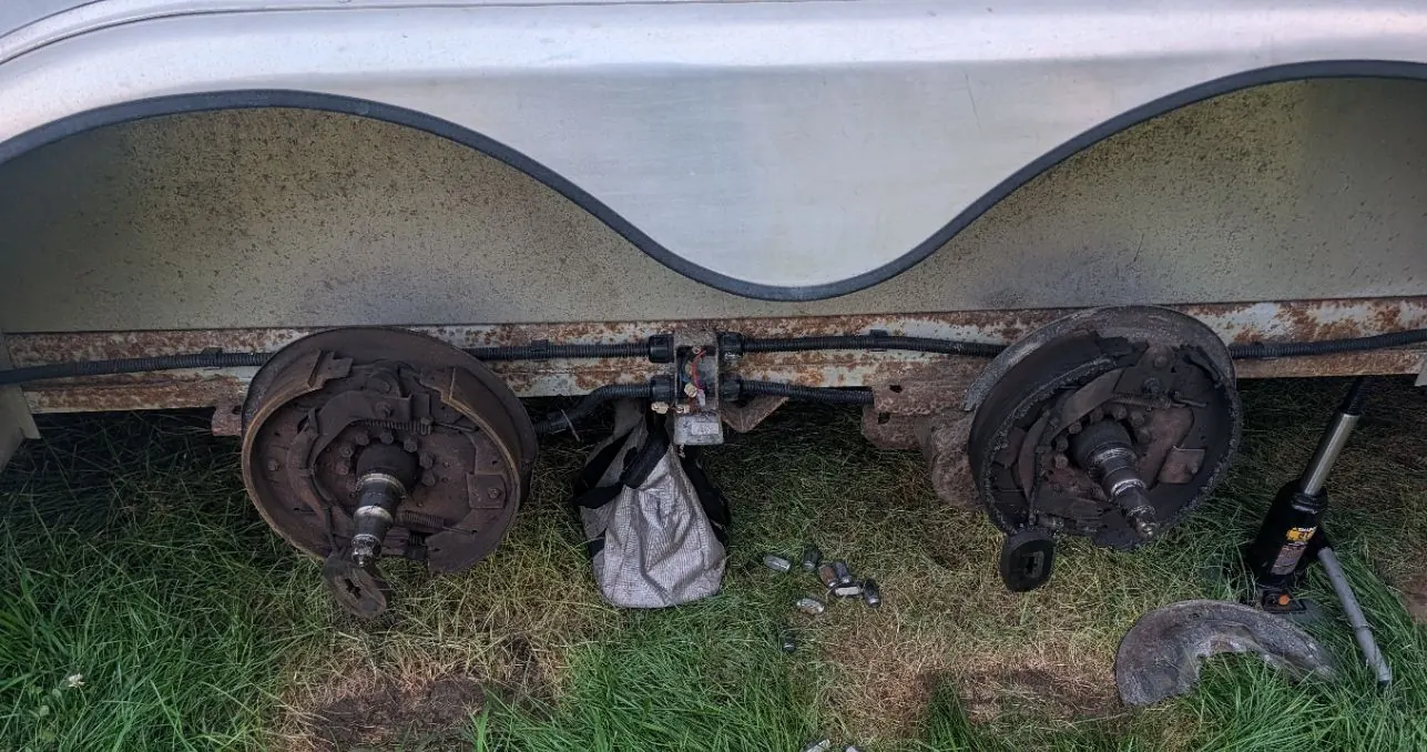Both wheels off a tandem axle trailer with the drums pulled and brake assemblies exposed