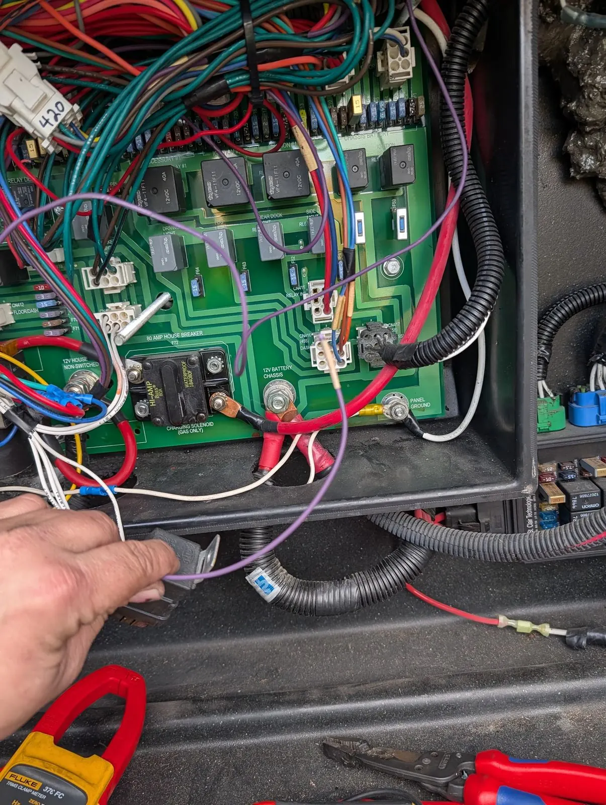 RV 12V power distribution panel opened for testing, with a clamp meter and hand tools alongside