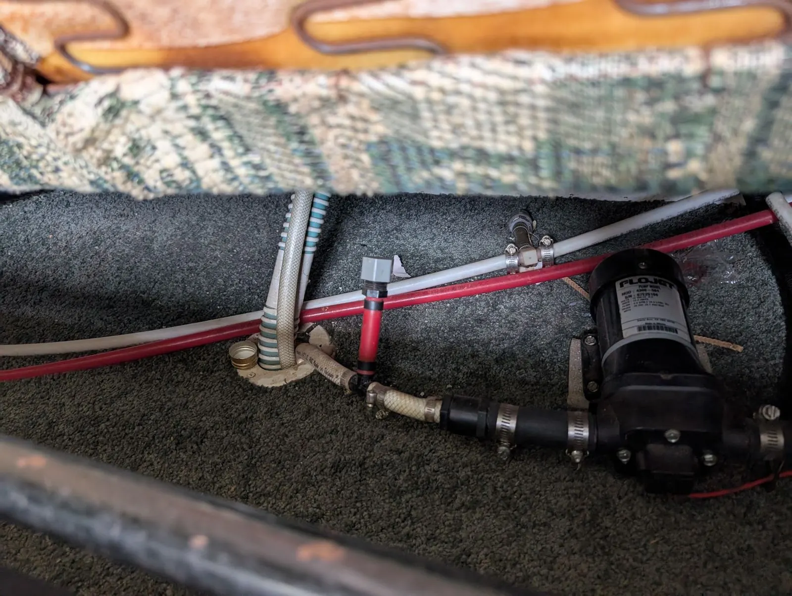 RV fresh water pump and PEX plumbing lines exposed under a dinette bench