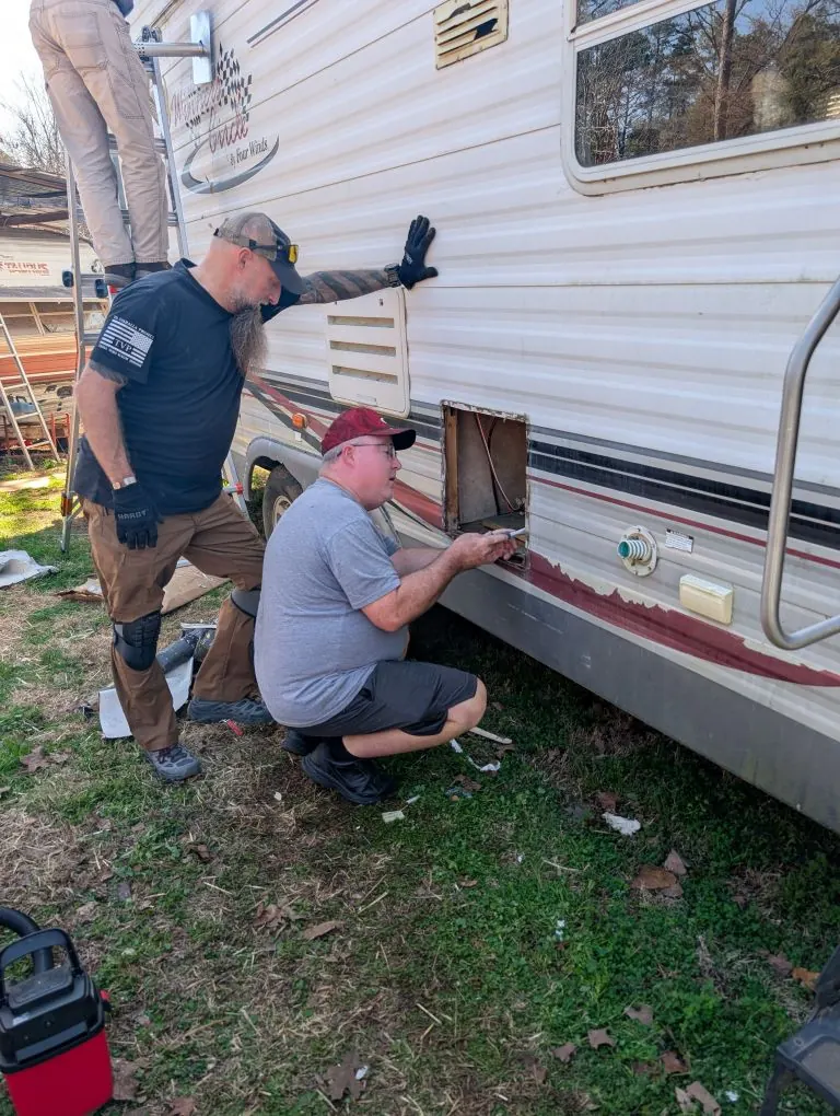 Two RV technicians replacing a water heater through the exterior access panel