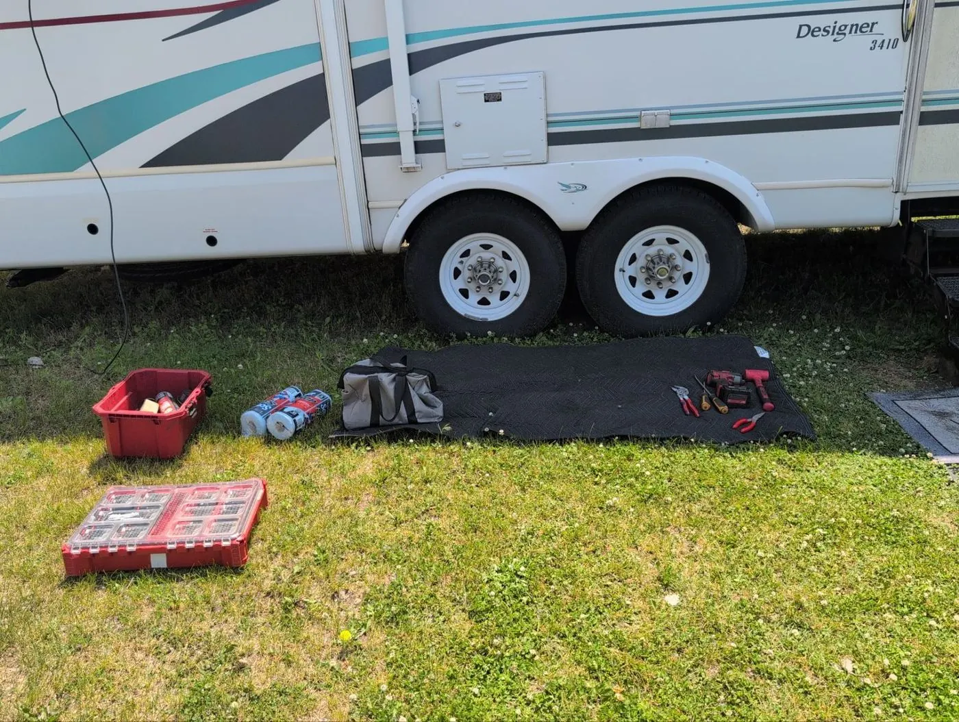 Fifth wheel trailer in a back yard with tool bags and parts laid out on a mat for a service call