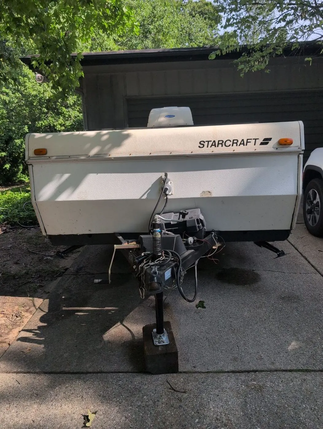Pop-up tent camper folded down in a driveway with the tongue jack raised