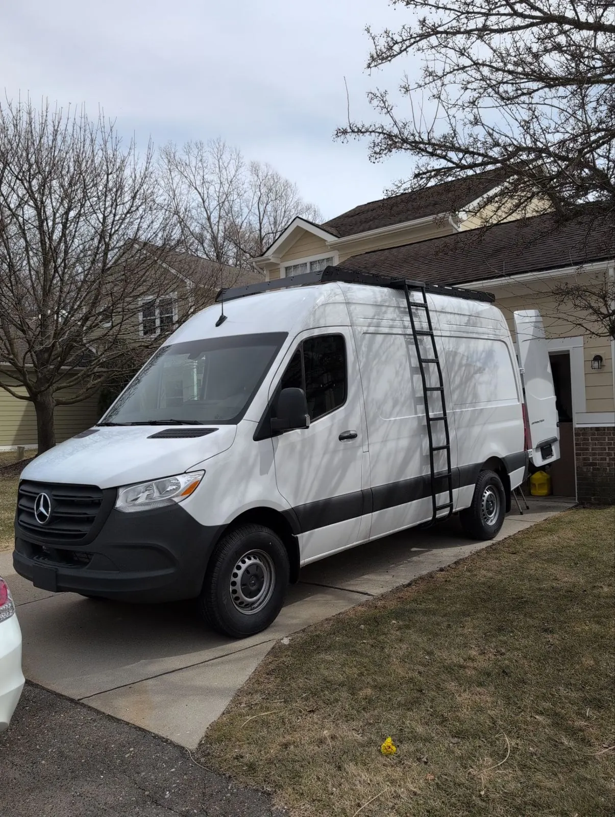 Mercedes Sprinter Class B camper van with a roof rack and ladder in a driveway